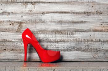Graceful bright red high-heeled female shoes stand on rough wooden background