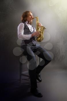 young saxophonist playing his bronze saxophone against a dark background