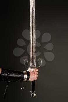 hand in armor holding a huge knightly sword on a dark background