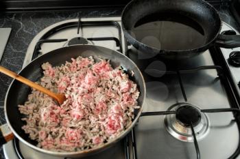Old pan with minced pork meat on the stove.