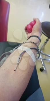 Detail of men's hand with a sticking needle during blood donation. Hand squeezing a red balloon.