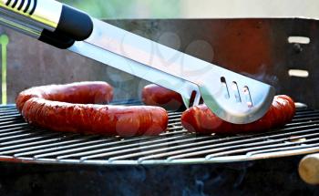 Rotating sausages with pliers on garden grill during barbecue.