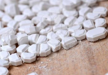 Macro of the white pills cut into pieces on wooden brown background.