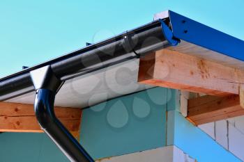 Closeup of a black steel roof rain gutter on a new house with insulated wall.