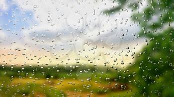 A view of the landscape through a wet window with digitally added of rain drops. Focused on rain drops on the glass, background with landscape is blurred, shallow depth of field.