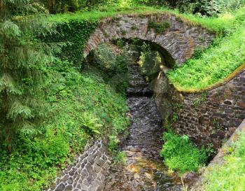 Wild stream flowing under an old stone bridge in nature.