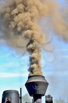 Vintage steam locomotive chimney is blowing out a smoke against the blue sky.