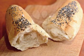 Two pieces of a white bread roll sprinkled with poppy seed and salt on a wooden cutting board.