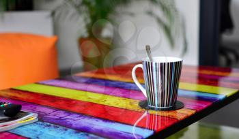 Multicolor glass table with cup of coffee in modern furnished living room. Focused on foreground with cup of coffee.