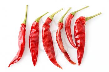 Top view of dried red hot chilli peppers arranged in a row on white background.