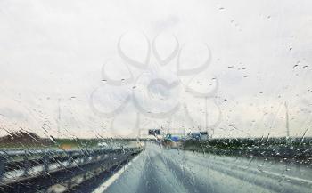 A view from car through window with rain drops during riding. Driving a car in the rain storm on highway.