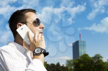 Successful Businessman Talking On The Phone In The Park With Corporate Office Building In The Background