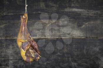 Smoked Chicken Leg Hanging on the Rope Against Wooden Background With Smoke