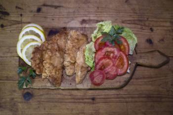Breaded Chicken Meat With Salad And Lemon Resting On a Rustic Wooden Board 