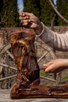 Whole Smoked Bacon Slab Held By Woman's Hand While Being Sliced With Butcher's Knife In A Rustic Environment. Delicious Domestic Food