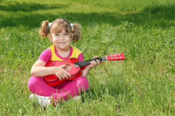 happy little girl with guitar sitting on grass 