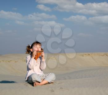 little girl play music on pan pipe in desert