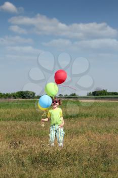 happy little girl with colorful balloons on meadow