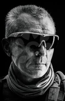 Close up black and white studio shot of special forces white-haired veteran in field uniforms, black background. Protective goggles glasses are on