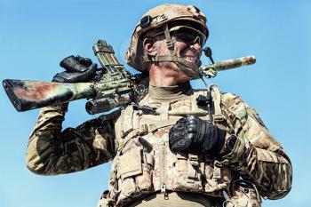 Half length low angle location shot of special forces soldier in field uniforms with weapons, portrait on blue sky background