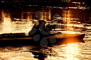 Silhouette of special forces man with rifle in army kayak. Boat moving calmly across the river, diversionary mission, sunset dusk