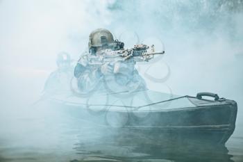 Special forces marine operators in camouflage uniforms paddling army kayak through river fog. Diversionary mission, machine gunner ahead