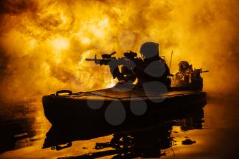 Backlit silhouette of special forces marine operators in military kayak on fire explosion background. Battle operation, bombs exploding