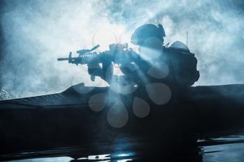 Backlit silhouette of special forces marine operators in military kayak on fire explosion background. Battle operation