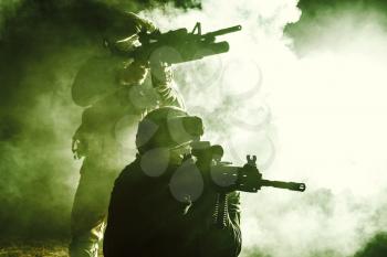 Black silhouettes of pair of soldiers in the smoke moving in battle operation. Back light, cropped, toned and colorized