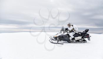Army soldier in winter camo somewhere in the Arctic moving across the snow field riding tracked snowmobile