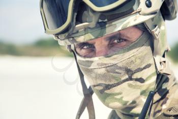 Close up, cropped portrait of airsoft, strikeball war games player, military or historical reenactment participant in tactical helmet replica, with hidden behind camouflage mask face looking at camera