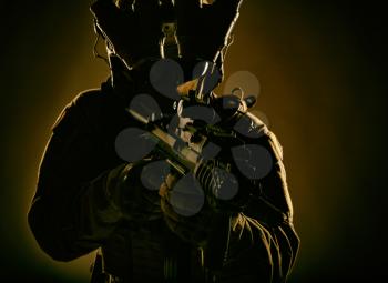 Special operations forces soldier, counter terrorism assault team fighter with night vision device on helmet and red dot laser sight on service rifle, low key studio shoot silhouette with backlight