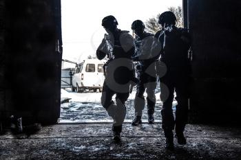 Silhouettes of police special operations forces tactical team, SWAT fighters aiming assault rifles while standing shoulder to shoulder in bright white doorway. Military tactical group storming room