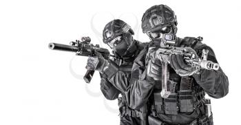 Two SWAT fighters, police special operations tactical group members in black uniform ans helmet, armed with assault rifles moving forward one behind another studio shoot isolated on white background