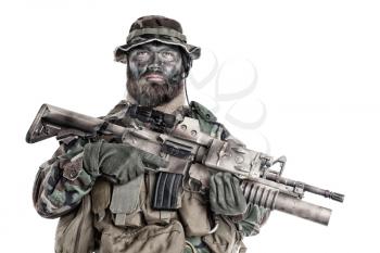 Serious commando fighter, military company mercenary with camouflage paint on bearded face, holding assault rifle with grenade launcher and laser sight, studio shoot isolated on white background