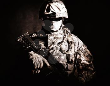 Half length portrait of special operations forces soldier, private military company guard in helmet, mask and uniform armed machine gun looking at camera. Contrast light, brown tone, black background