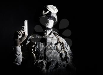 Elite troops fighter, US special operations forces soldier, marine in combat uniform and ammunition with hidden behind mask and glasses face standing in darkness with raised up service pistol in hand