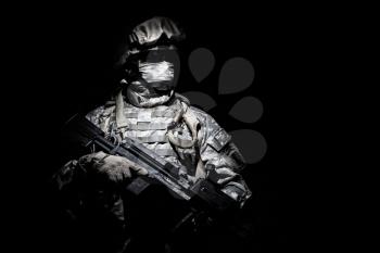 United States Armed Forces soldier in battledress with black glasses and mask on face, armed squad automatic weapon emerges from darkness. Military threat, secret stealth mission, hybrid war combatant