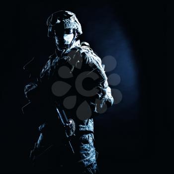 Armed and equipped soldier hiding his identity with balaclava and glasses during secret military, counter terrorist, security operation. Studio shot with high contrast backlight on black background