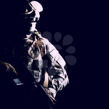 Armed army soldier in camouflage uniform, with hidden face, sneaking in dark during combat, counter terrorist raid. Secret military operation, stealth mission under cover of darkness, night patrol