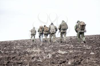 Army soldiers on march. Elite forces fighters group, commando tactical unit, reconnaissance team members in camouflage uniform, walking in line, carrying backpacks on muddy terrain