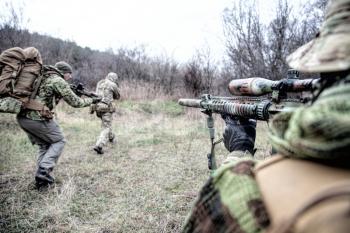Modern warfare combatants group, commando fighters squad, team members attacking, rushing trough woodland. Sniper or marksman covering comrades in forest, over shoulder view