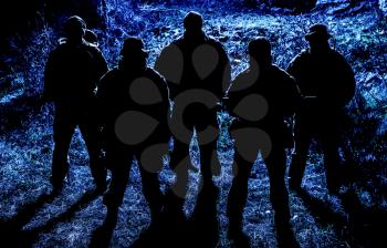 Group of armed soldiers, modern military mercenaries, secret service fighters, army special operations riflemen, commandos crew standing together in line in darkness, patrolling area at nighttime