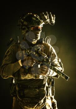 Anti-terrorist squad fighter, army elite forces soldier in combat uniform and tactical ammunition, armed mini submachine gun, wearing night-vision device, low key studio portrait on black background