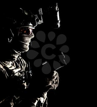 Army elite commando, professional mercenary, counter-terrorist tactical team fighter in combat helmet, equipped night-vision device, creeping in darkness with service pistol in hand, studio shoot