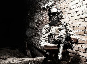 Special operations forces soldier, counter terrorism assault team fighter with night vision device on helmet and service rifle, low key indoor shot brick wall