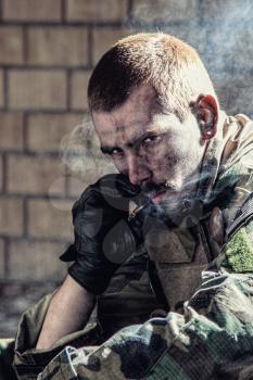 Handsome soldier sitting in ruined building smoking cigarette staring at the camera