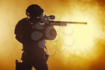 Studio shot of swat police operator with sniper rifle in black uniforms pointing criminals terrorists Fire smoke screen background. Punishment concept