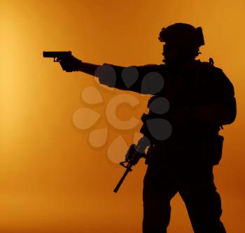 United states Marine Corps special operations command Marsoc raider with weapon aiming pistol. Silhouette of Marine Special Operator orange background