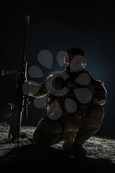 Army sniper with big rifle sitting holding rifle on black background